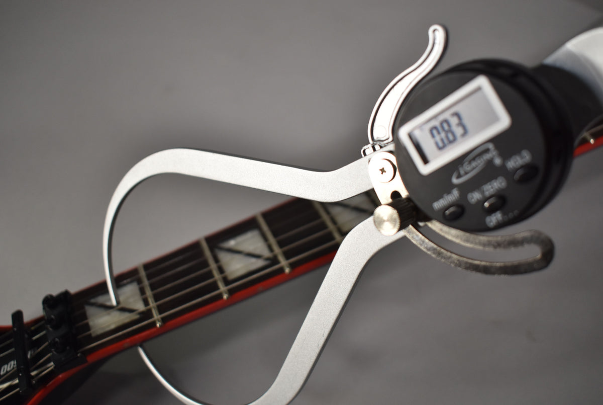 Close-up of the guitar's fretboard with block inlays, showing a digital caliper measuring the string height at 0.83mm.