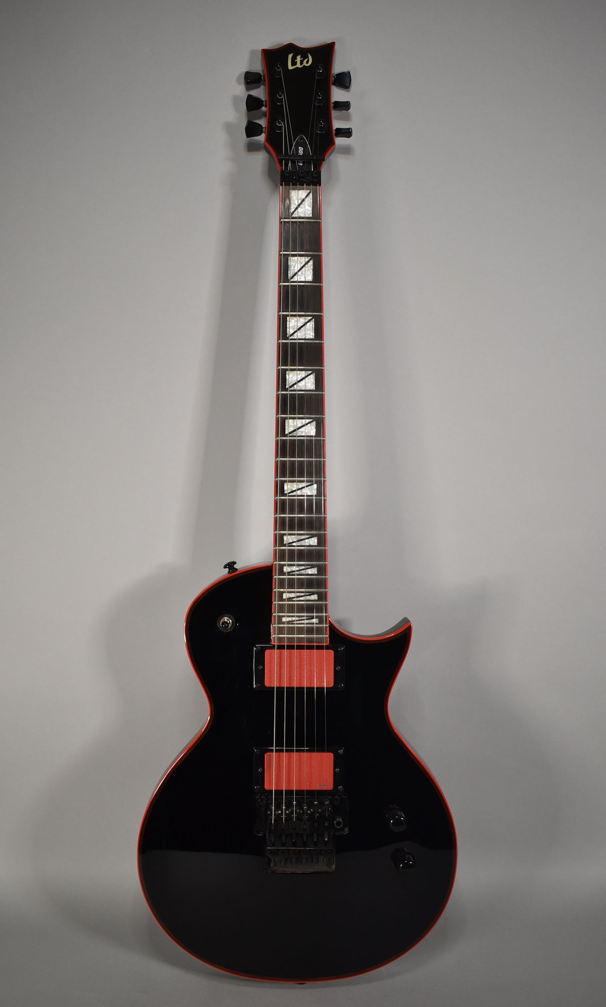 Full-length, front view of a black electric guitar with a glossy finish, red binding, red pickup covers, and rectangular fret inlays.