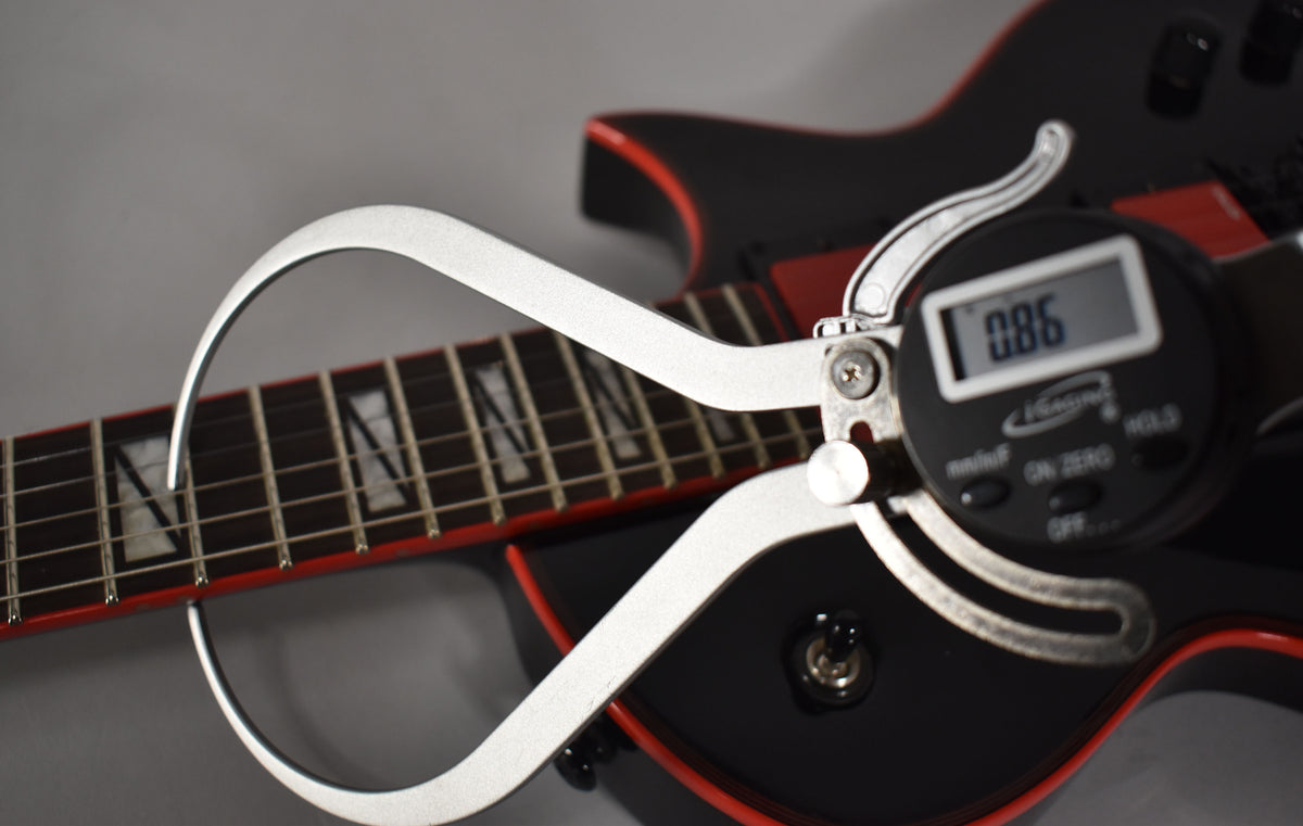 A digital caliper measures the fret height on the black guitar's neck, showing "0.86" on its display.