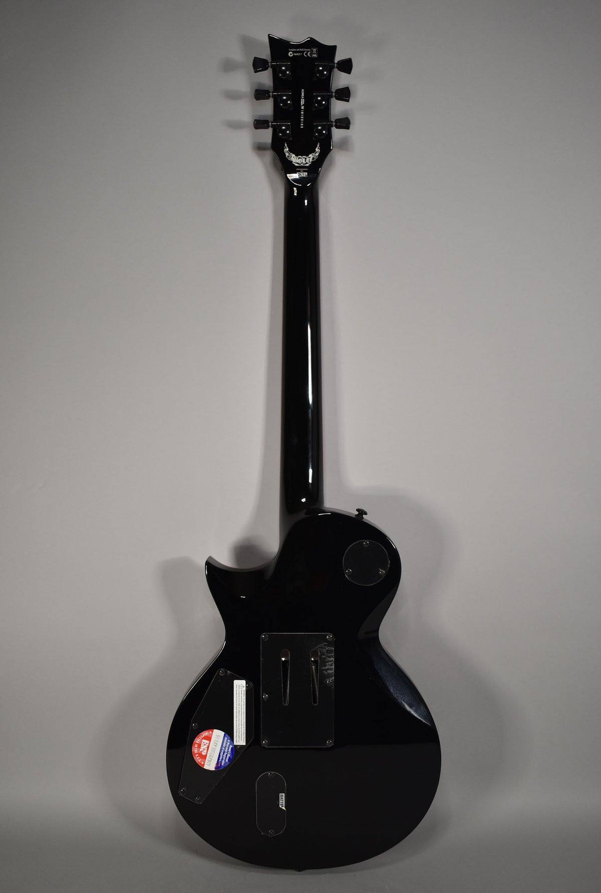 The back of a glossy black electric guitar, showing the headstock, neck, and body with control and battery covers.