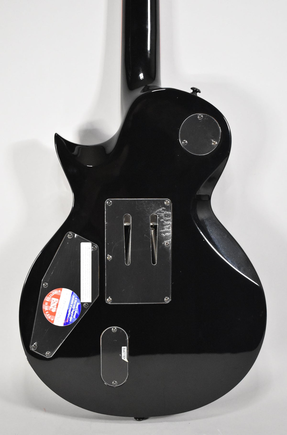 The guitar's glossy black back shows a tremolo spring cavity cover with visible wear, a control cavity cover, and a battery compartment.