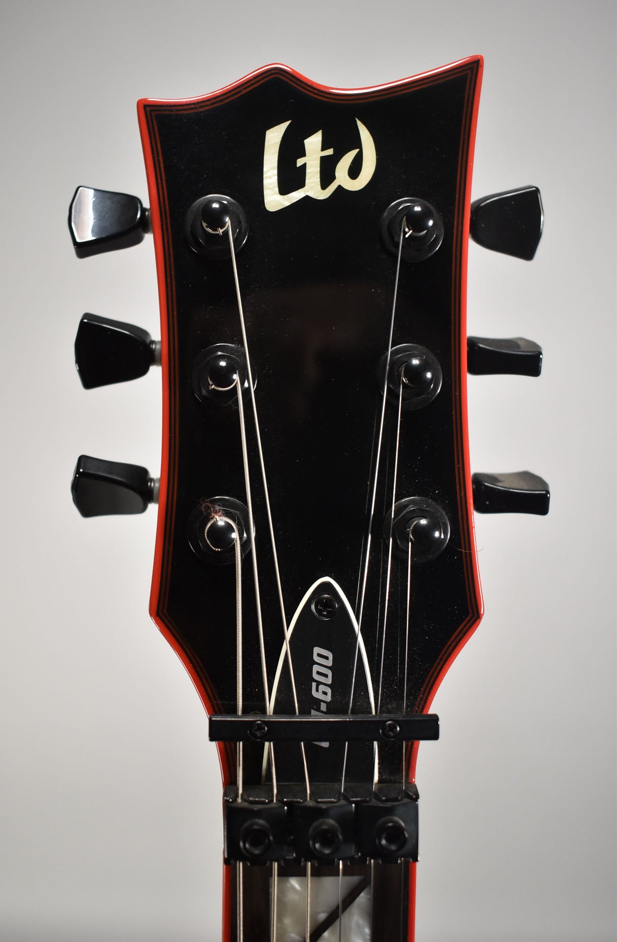 The guitar's black gloss headstock with red binding and black tuners is framed from above, showing the locking nut and string tree.