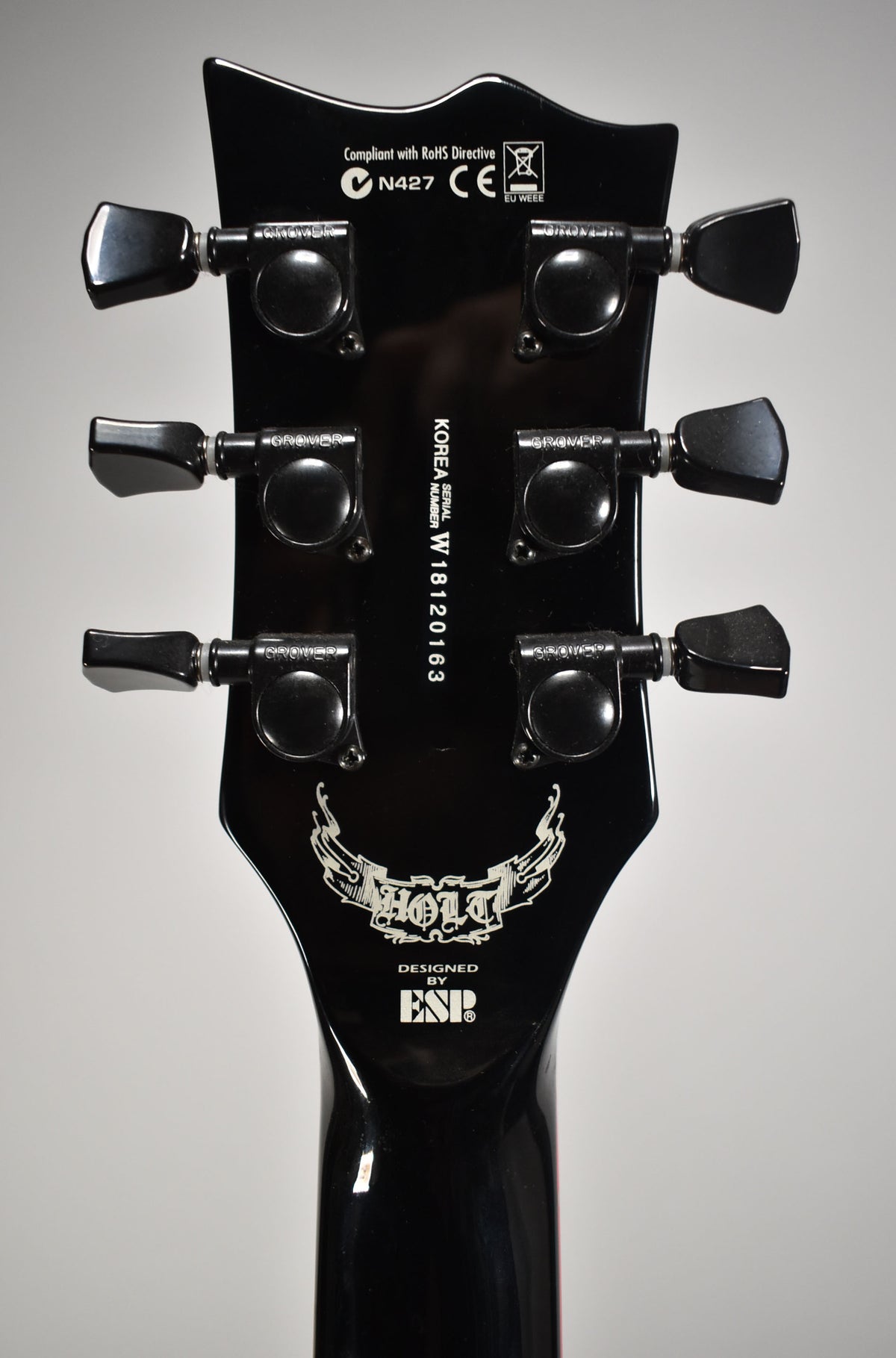 The guitar's glossy black headstock, viewed from the rear, features six black Grover tuners and a white "HOLT" graphic.