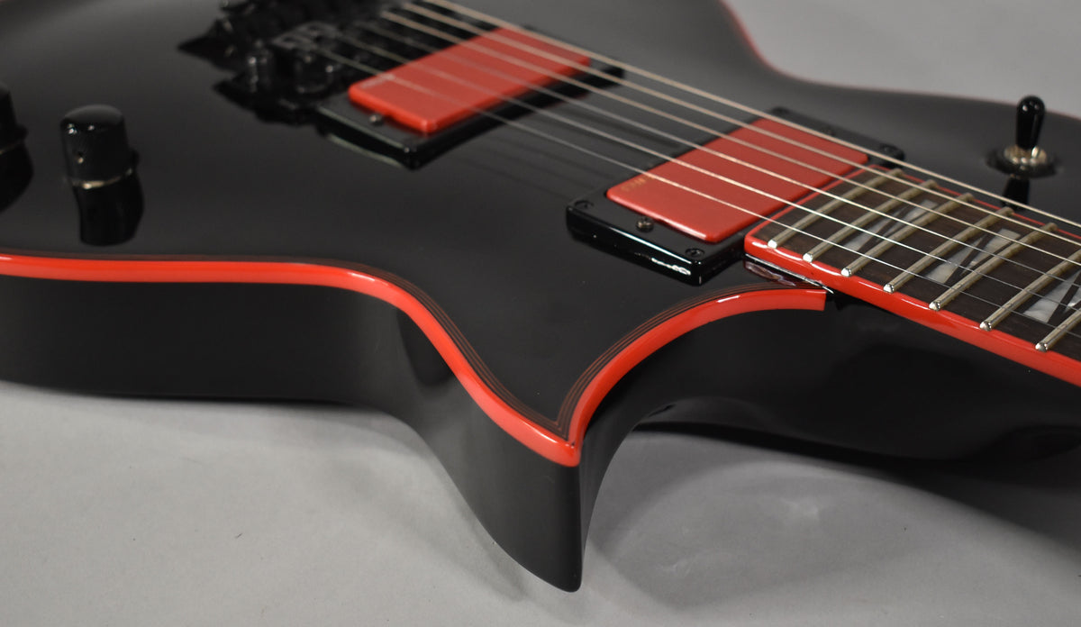 Close-up of the black guitar body with red binding, showing two red humbucker pickups and a volume knob.