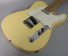Angled view of a vintage white Telecaster body, showing the chrome bridge, control plate with two knobs, and a white pickguard.