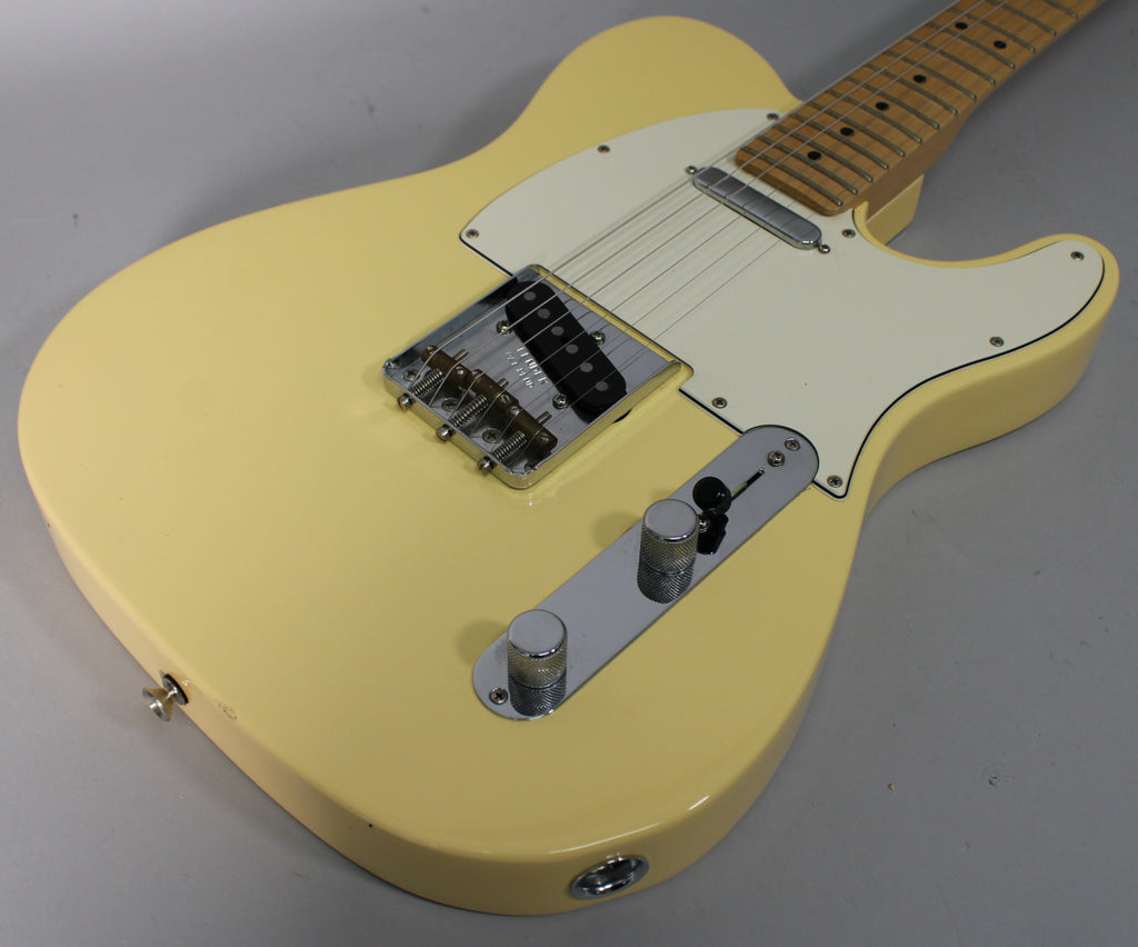Angled view of a vintage white Telecaster body, showing the chrome bridge, control plate with two knobs, and a white pickguard.