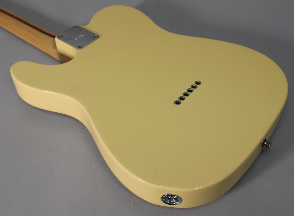 The back of a vintage white Telecaster body, showing string-through ferrules, a chrome neck plate, and output jack.