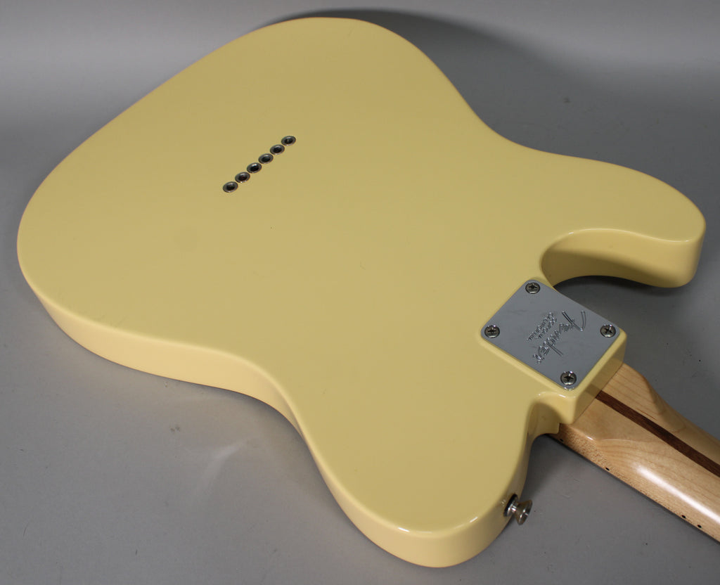 Rear view of a vintage white Telecaster body, showing the neck plate, output jack, and six string-through-body ferrules.
