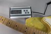 The guitar's weight, 7.12 lbs, is displayed on a digital scale, with the maple fretboard and vintage white body visible.