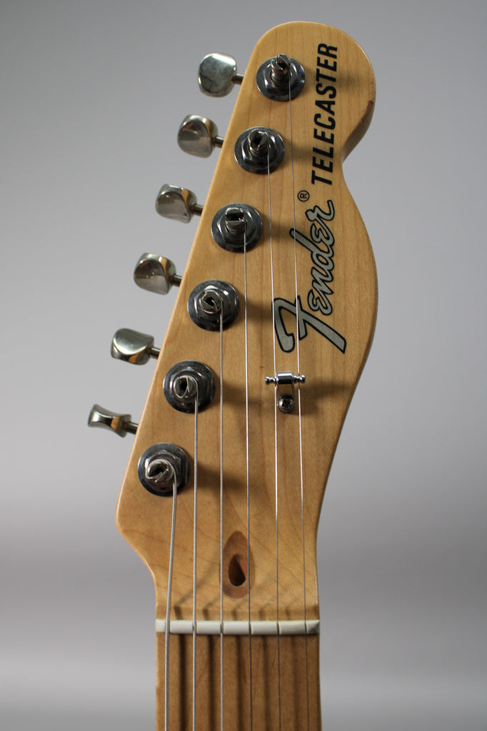 Close-up of the natural wood headstock, angled left, showing six chrome tuners, a string tree, and the nut.