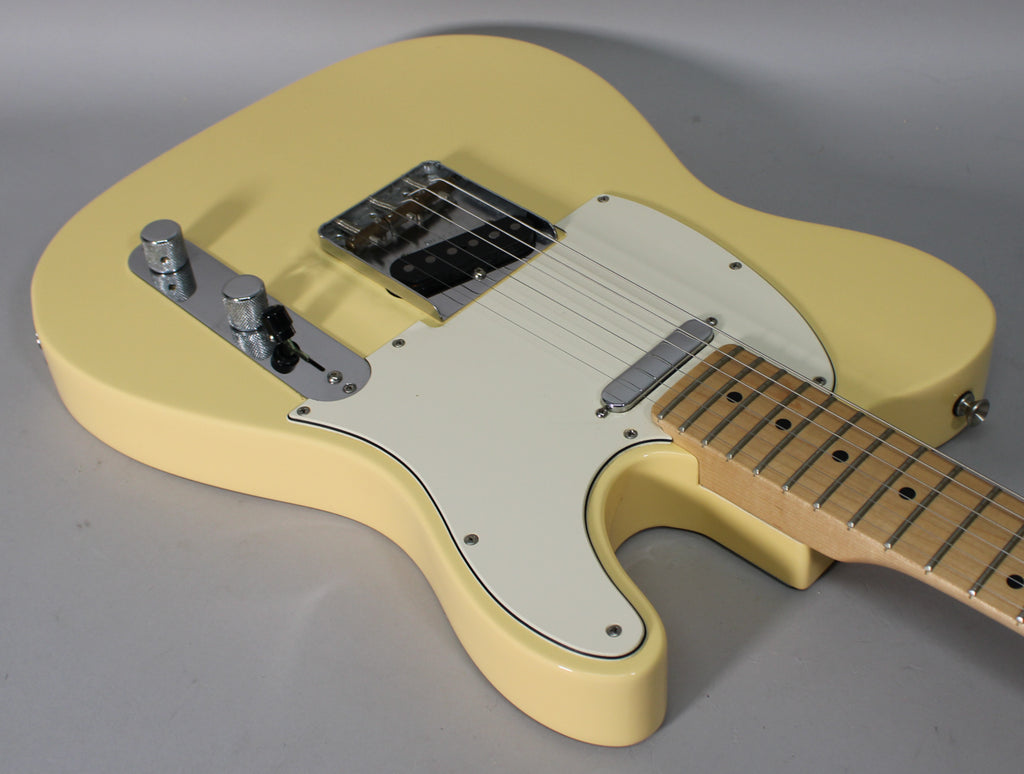 The vintage white Telecaster body is angled, showing the chrome bridge, control plate with two knobs, and a maple fretboard.