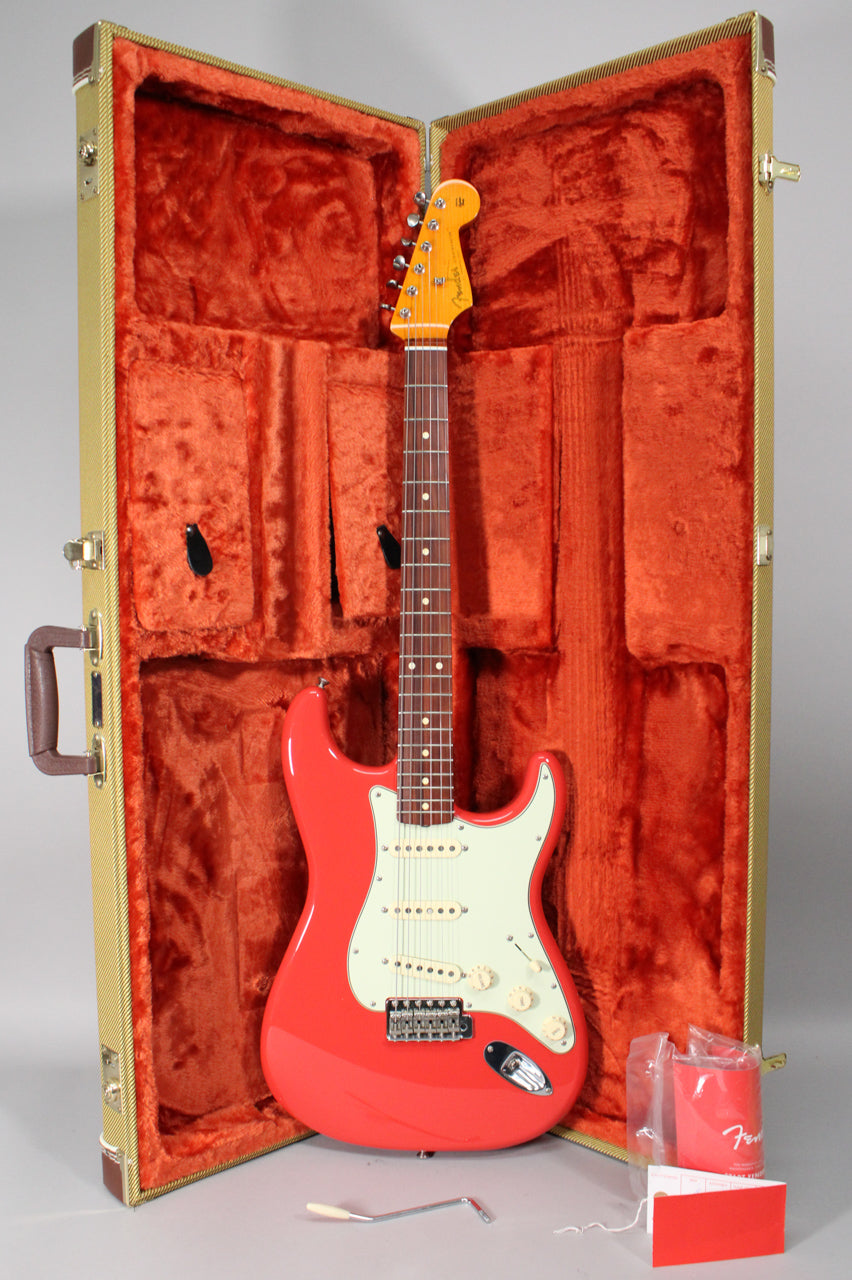 Full-length view of a glossy red Stratocaster with a white pickguard and light brown neck, standing in an open tweed hard case.