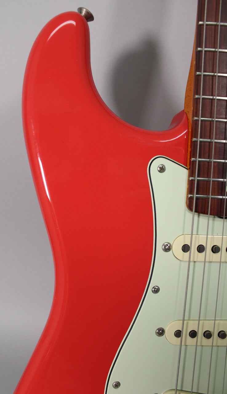 Close-up of the upper horn and cutaway of a glossy Fiesta Red Stratocaster, with a mint green pickguard and cream pickups.