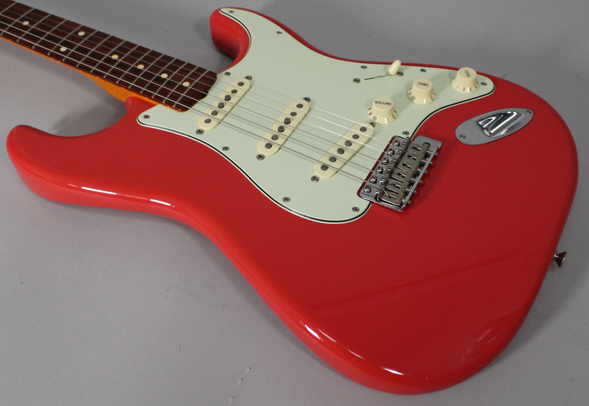The Fiesta Red Stratocaster body, angled from the neck, shows a mint green pickguard, three cream single-coil pickups, and chrome hardware.