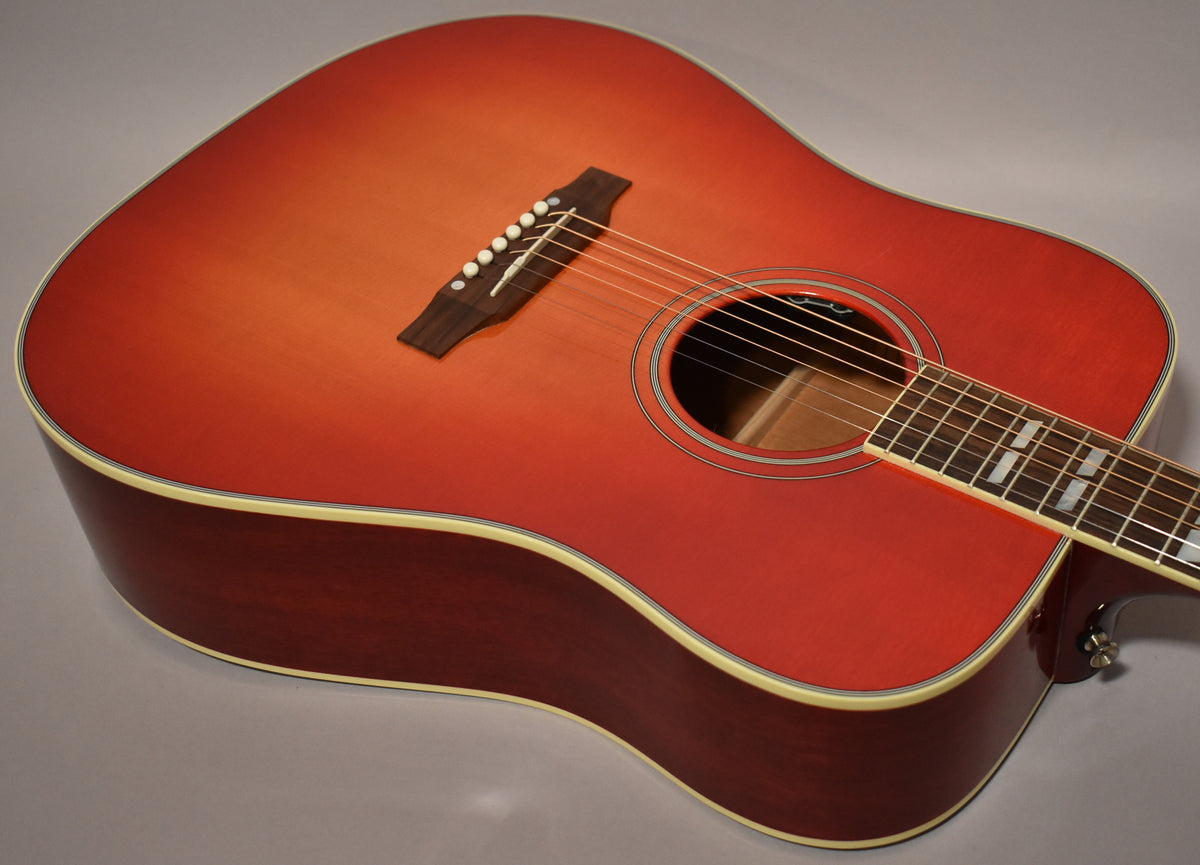 The cherry sunburst acoustic guitar's body is angled, showing the soundhole, bridge, and part of the fretboard with block inlays.