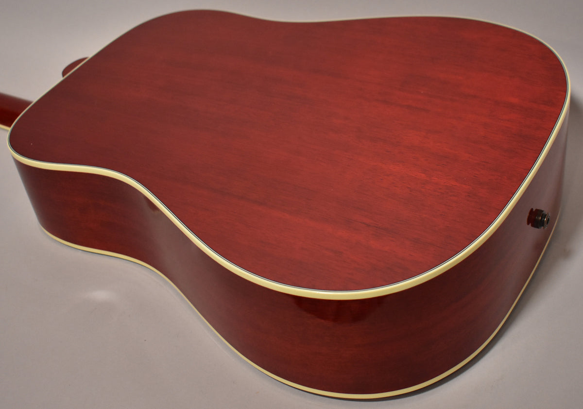 The back and lower bout of a cherry sunburst acoustic guitar, showing the output jack and cream binding.