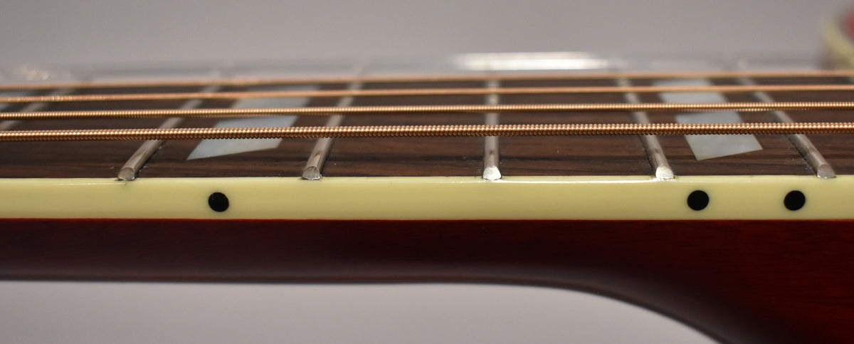 Close-up of the guitar's fretboard and neck binding, showing trapezoid inlays, side dots, and copper-colored strings.