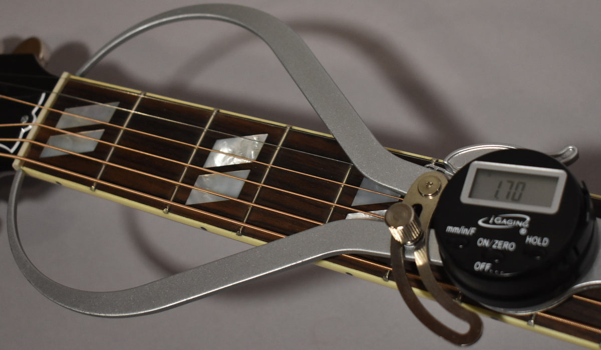 A digital caliper measures the string height above the dark fretboard with mother-of-pearl parallelogram inlays.