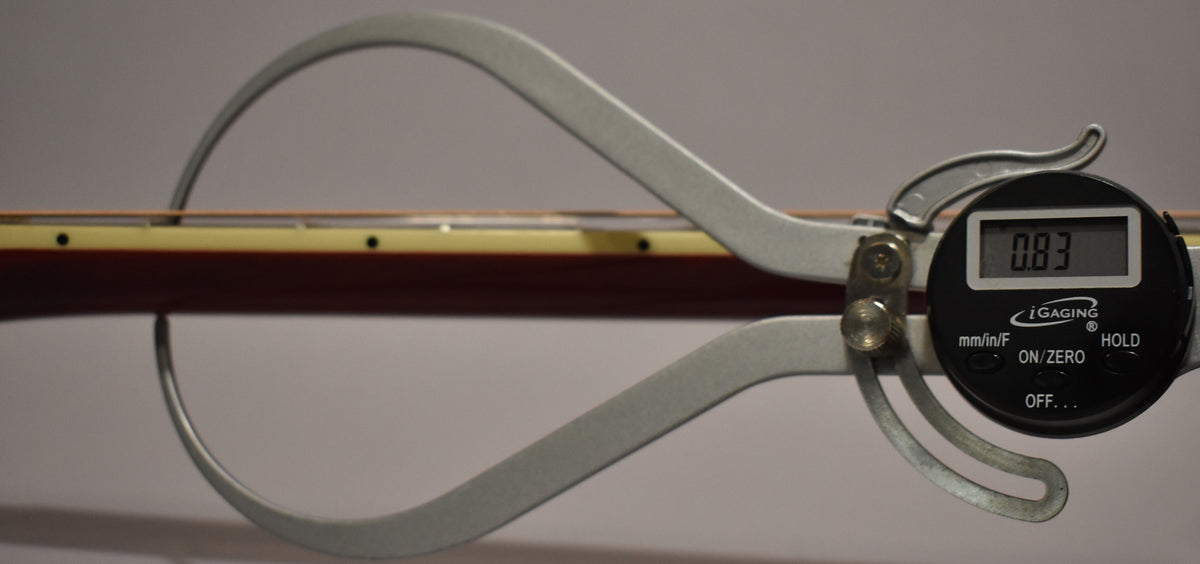 A digital caliper measures the guitar's neck thickness at 0.83 inches, showing the dark cherry sunburst neck and cream binding.
