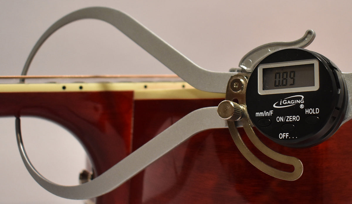 A digital caliper measures the guitar's cherry sunburst body and neck, displaying "0.89" on its screen.