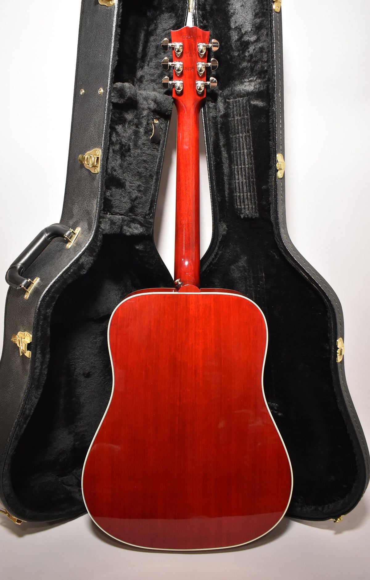 The guitar's cherry sunburst back and neck are visible, with six chrome tuners on the headstock, standing in its open black hard case.