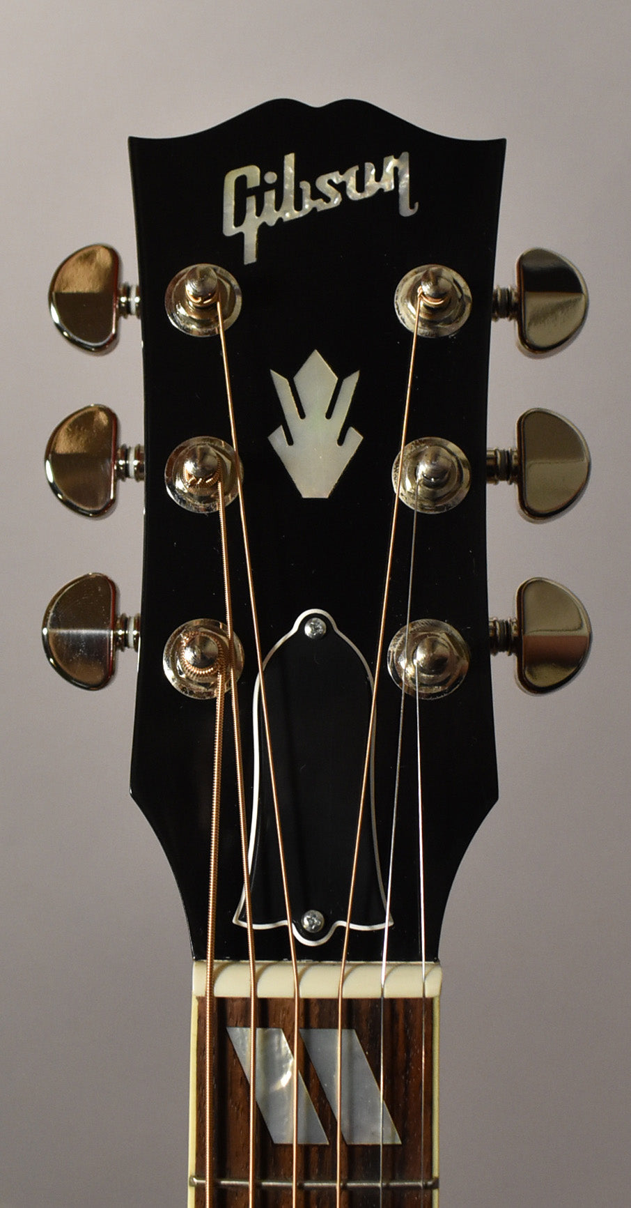 Close-up of the black headstock with gold tuners, showing the top of the fretboard with parallelogram inlays.