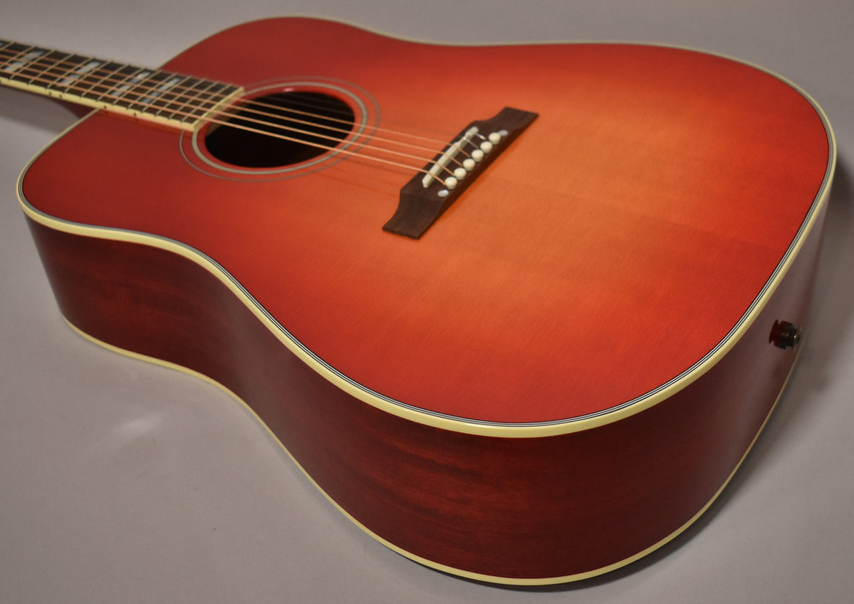 The guitar's cherry sunburst body, with a dark brown back and sides, is angled to show the bridge, soundhole, and endpin jack.
