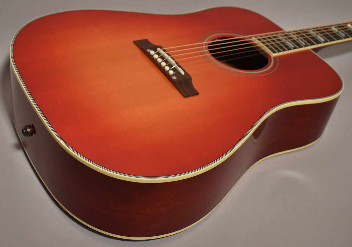 The cherry sunburst acoustic guitar is angled from the lower left, showing the body, soundhole, bridge, and output jack on the lower bout.