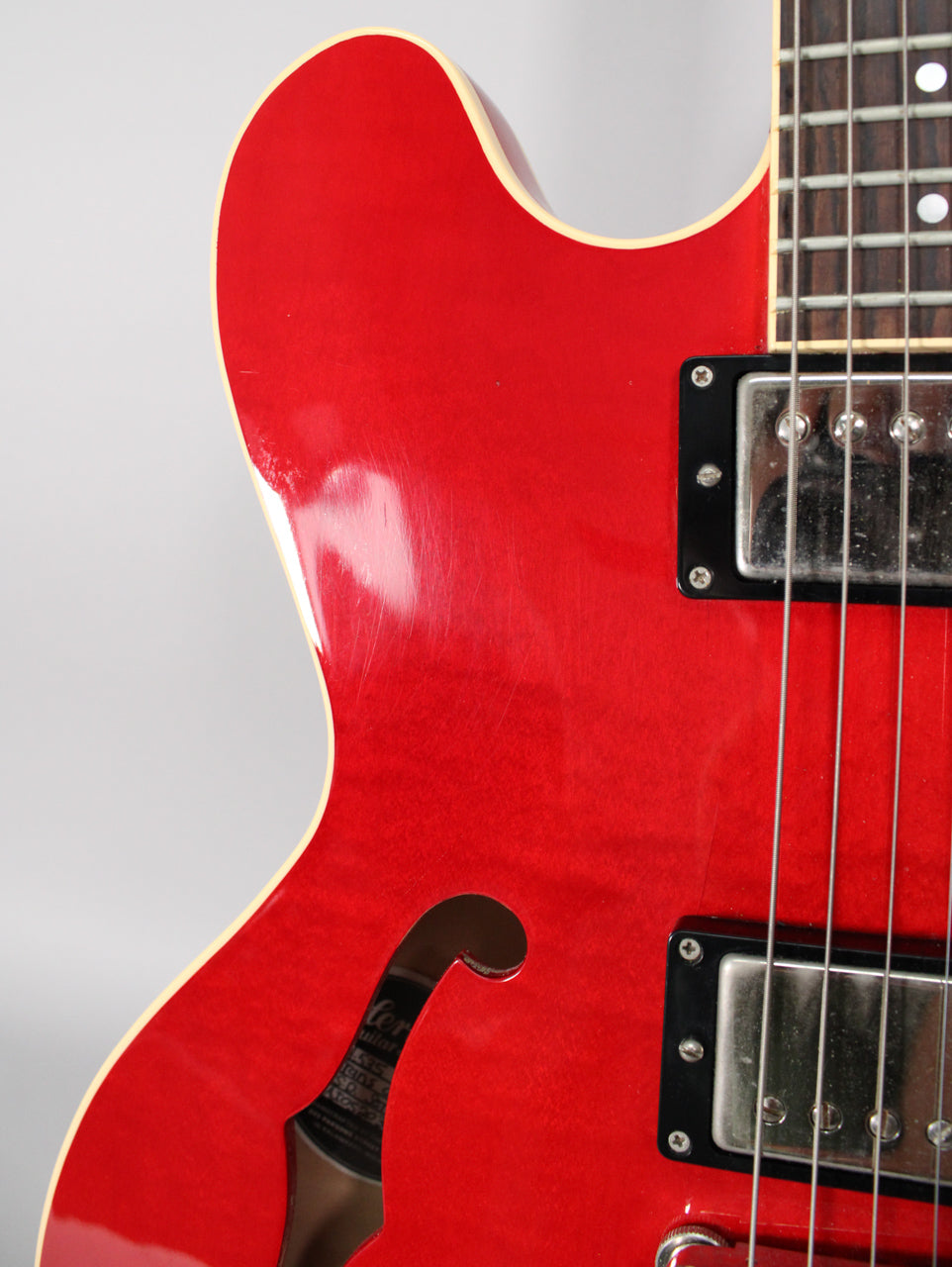 Close-up of the upper body of a trans red semi-hollow guitar, showing the f-hole, bridge pickup, and light surface scratches.