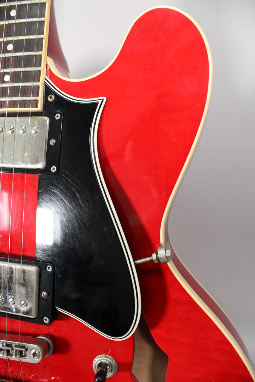 Close-up of the upper bout of a trans red semi-hollow guitar, showing the black pickguard with heavy pick scratches and chrome hardware.