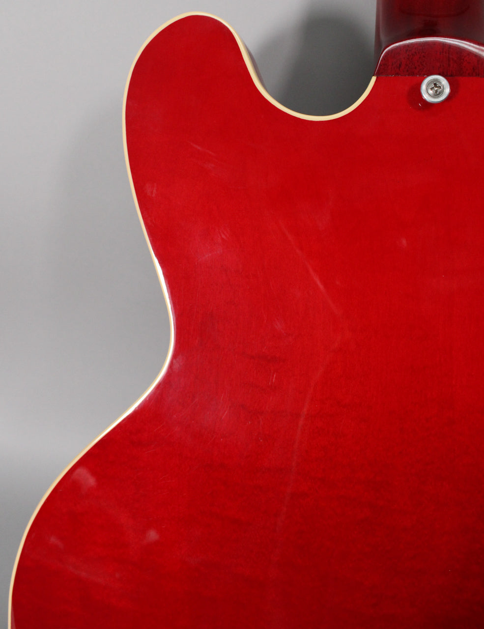 Close-up of the guitar's trans red back, showing light surface scratches, a cream binding, and a strap button near the neck joint.