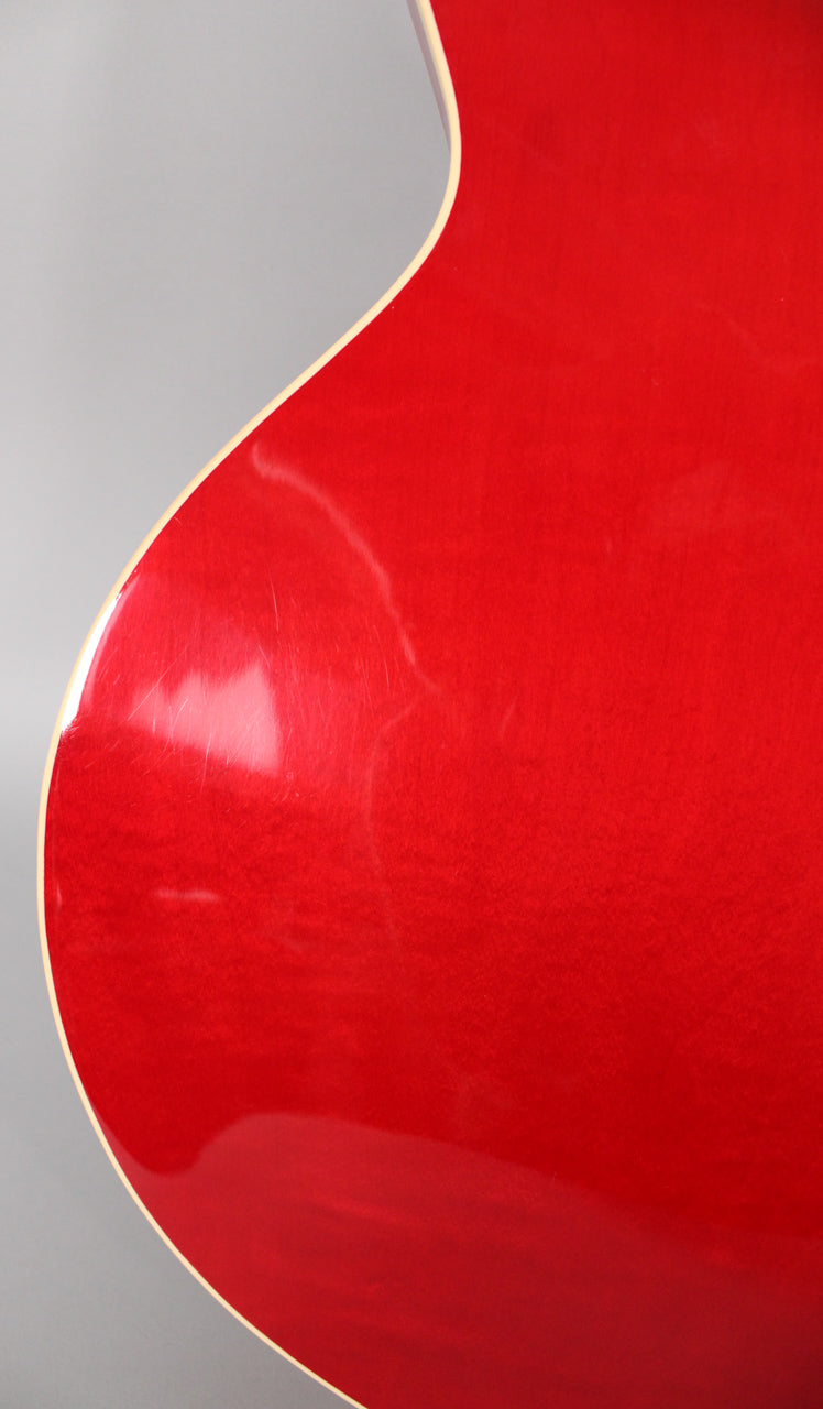 Close-up of the guitar's upper bout, showing the translucent red finish with visible light scratches and cream binding along the edge.