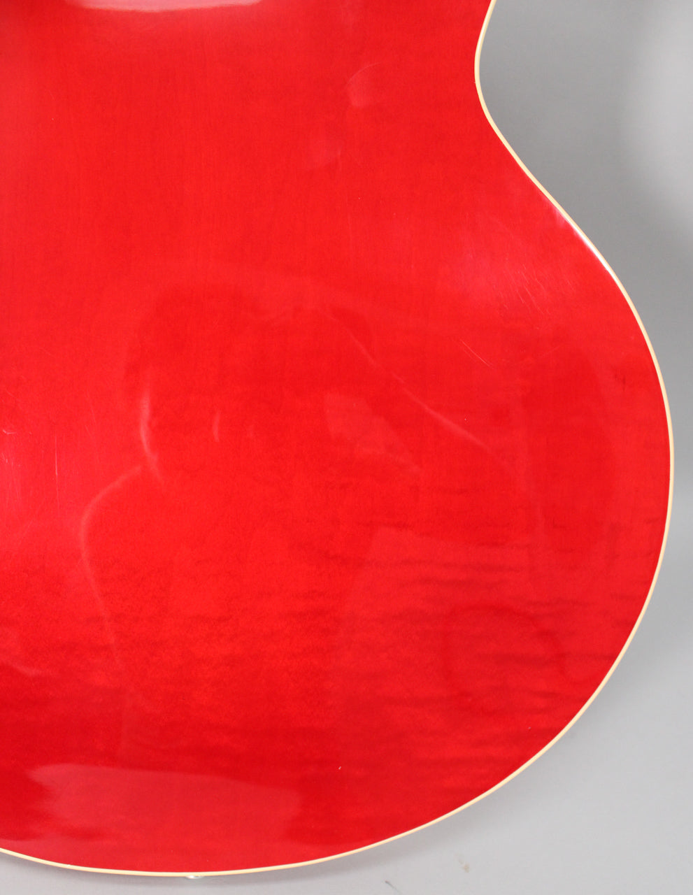 Close-up of the guitar's trans red back, showing subtle wood grain, light surface scratches, and cream binding along the curved edge.