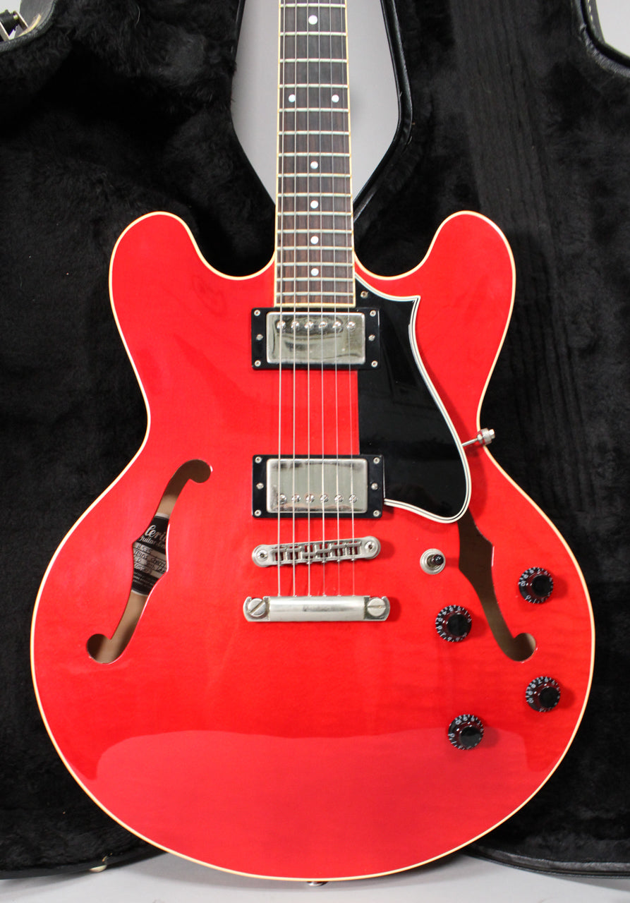Full-frame view of a glossy red semi-hollow guitar with cream binding, black pickguard, two humbuckers, and four black control knobs.