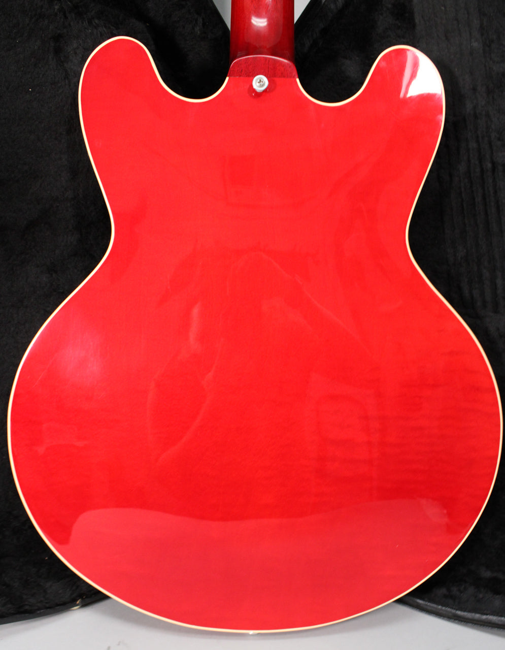 The back of a glossy trans red semi-hollow guitar, showing the neck joint and subtle wood grain through the finish.
