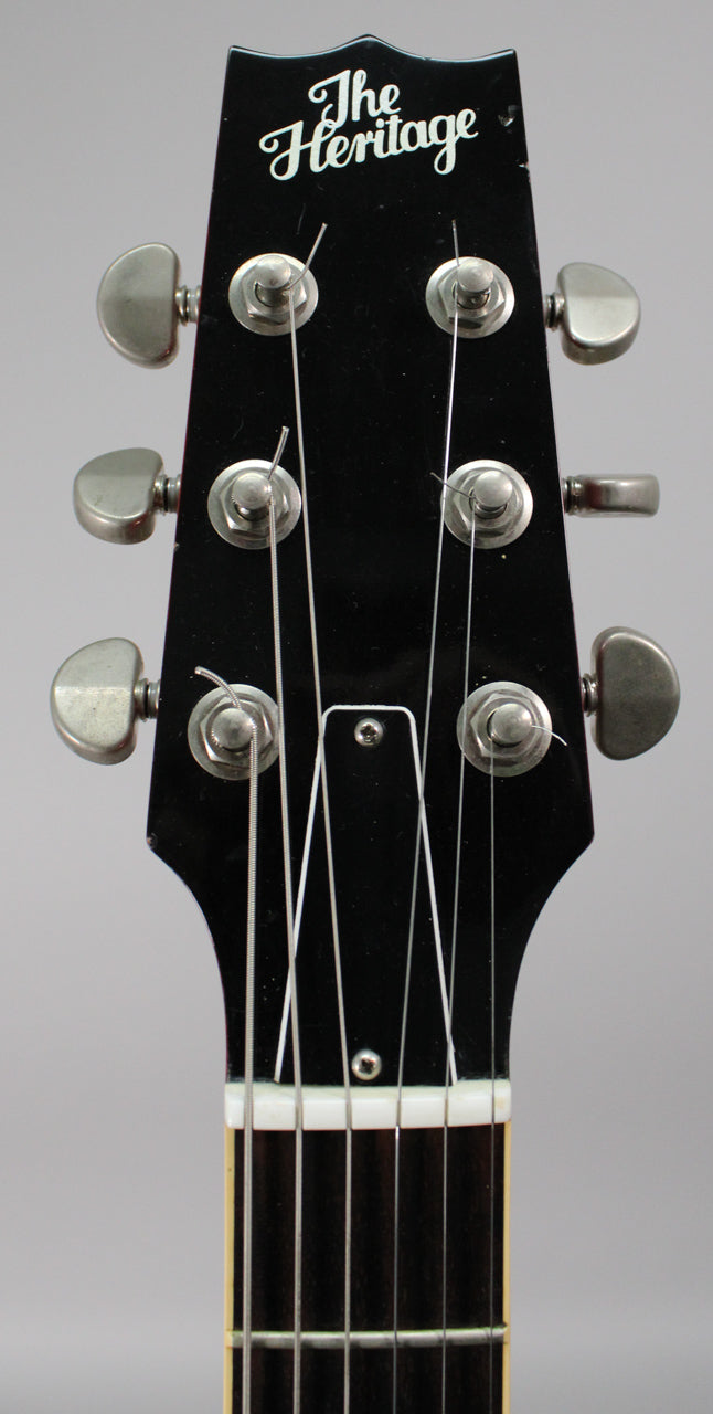 Close-up of the glossy black headstock, showing six chrome tuners, a white nut, and the top of the fretboard.