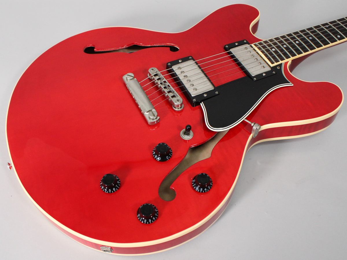 The semi-hollow guitar's glossy trans red body, with cream binding, shows two humbuckers, a black pickguard, and four black control knobs.