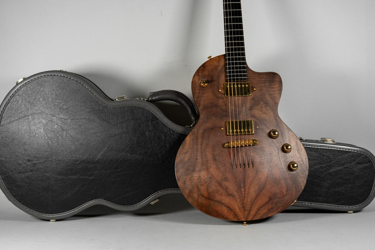 Full view of the guitar's figured walnut body and gold hardware, with its black hard case open behind it.
