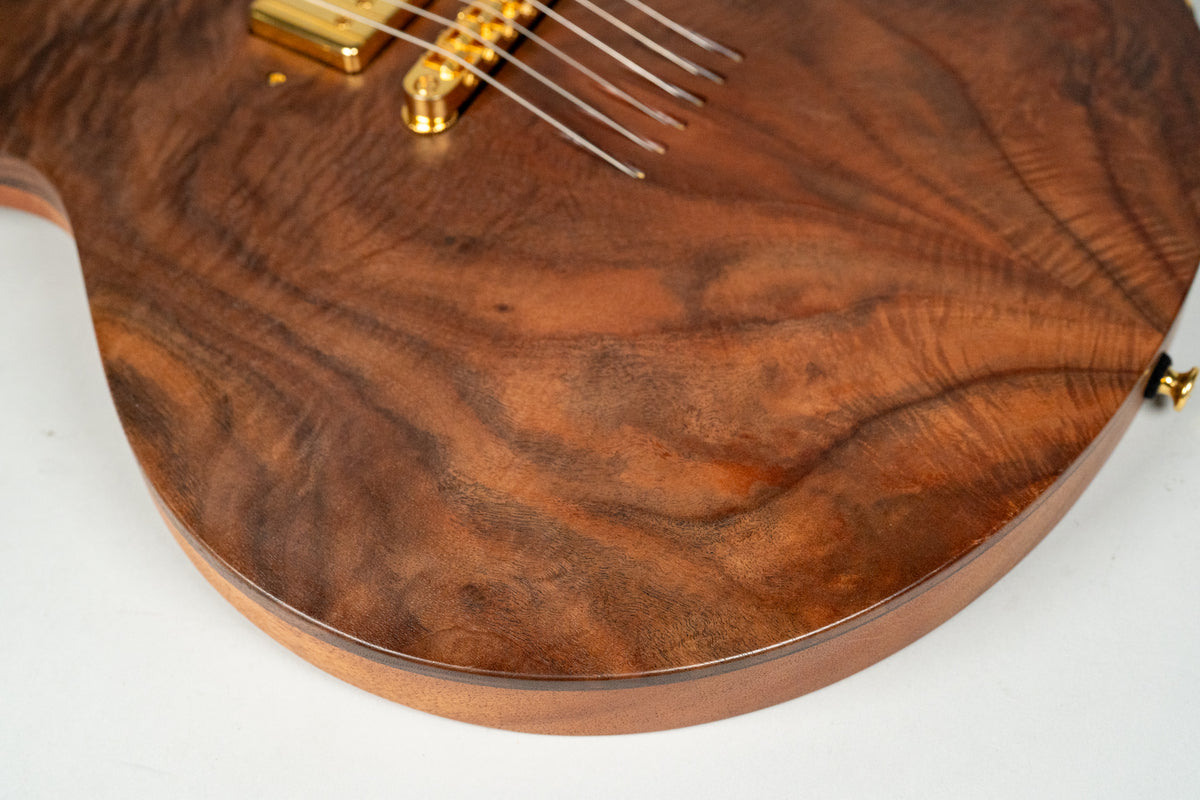 Close-up of the guitar's lower bout, showing the figured walnut top with a satin finish and gold hardware, including a bridge pickup.