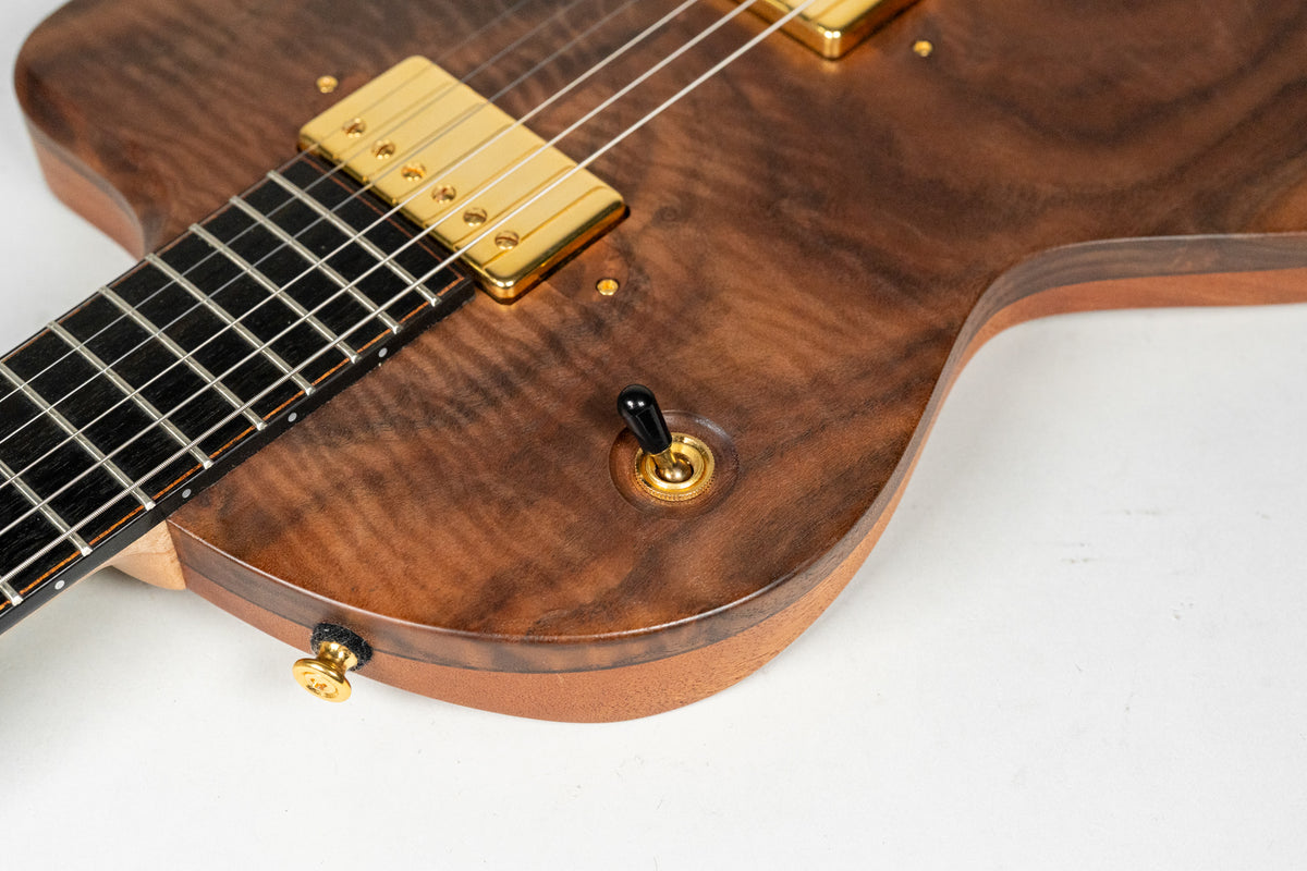 Close-up of the guitar's body, showing the dark figured walnut top, gold humbucker pickups, and a black-tipped gold toggle switch.