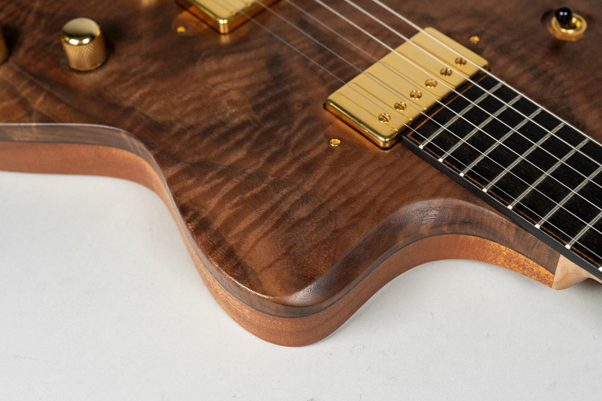 Close-up of the guitar's lower bout, showing the figured walnut top, gold humbuckers, and a single gold knurled control knob.