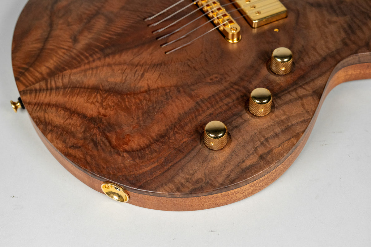 Close-up of the guitar's lower bout, showing the figured walnut top, three gold knurled control knobs, and a gold output jack.