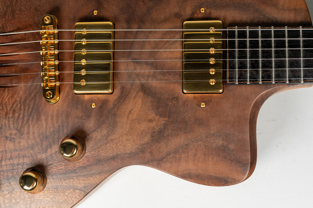 Close-up of the figured walnut body, showing gold humbuckers, bridge, and two knurled control knobs, with the fretboard visible.