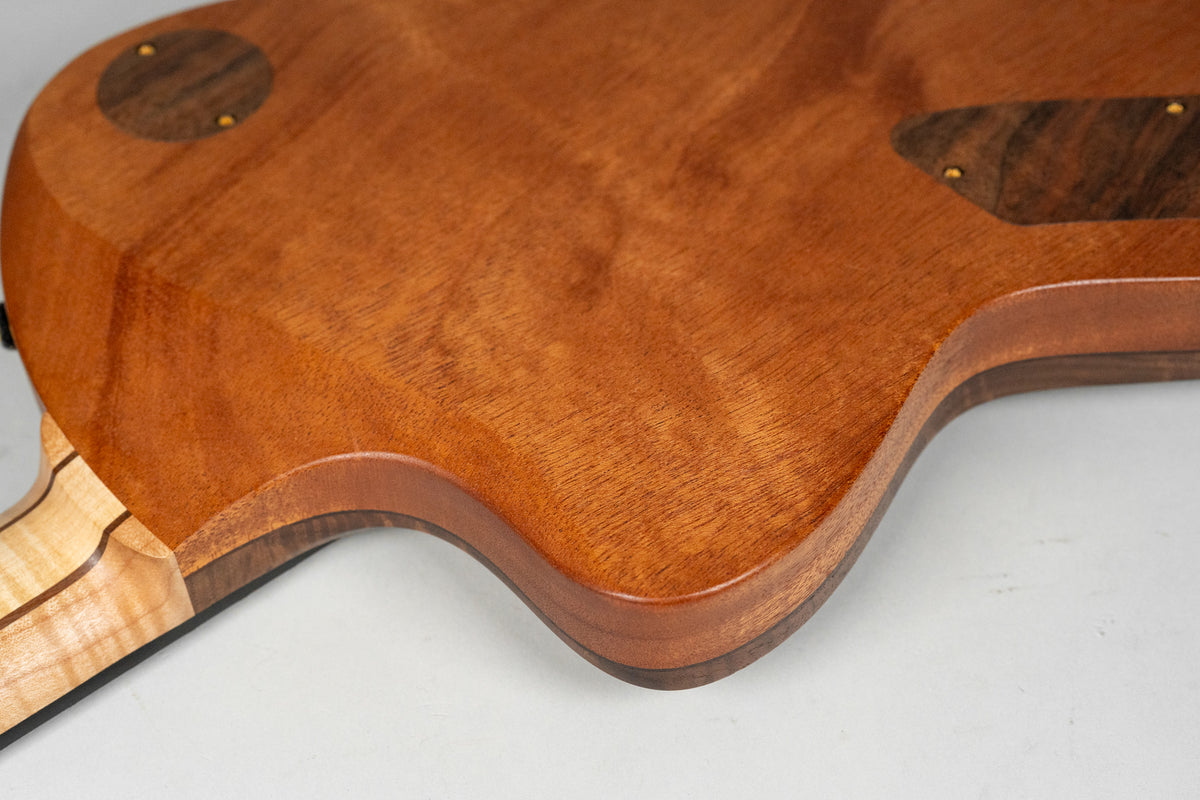 Close-up of the guitar's back, showing the figured walnut body with a smooth, glossy finish and a light-colored maple neck.
