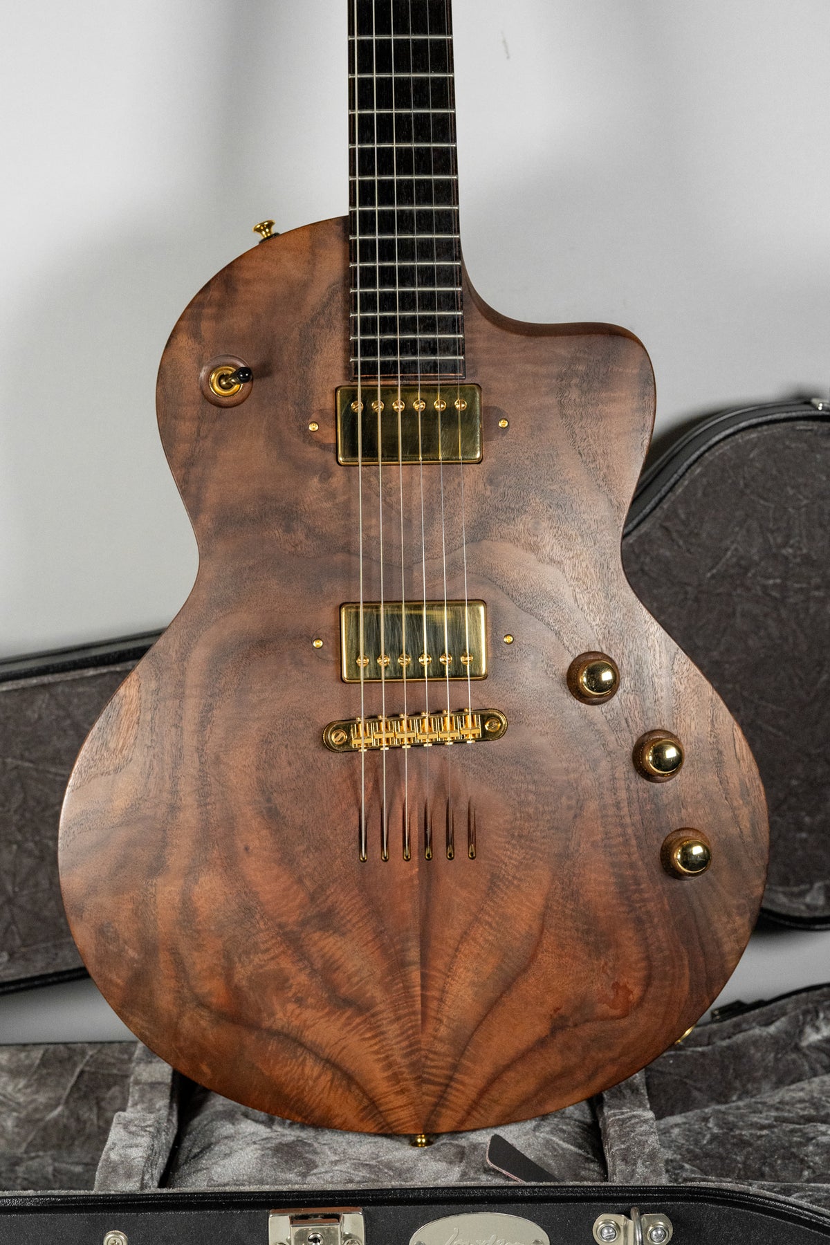 Full-frame view of a dark walnut electric guitar with a figured grain, gold hardware, and three gold control knobs.