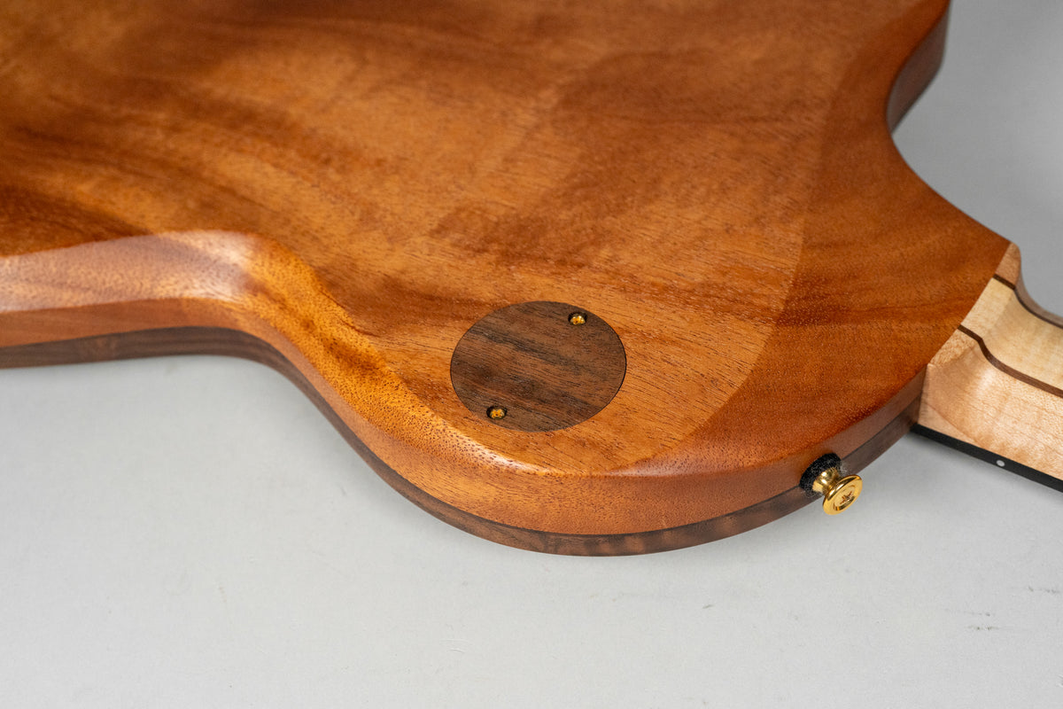 The guitar's figured walnut back, with a circular control cavity cover and gold output jack, shows a multi-piece neck joint.