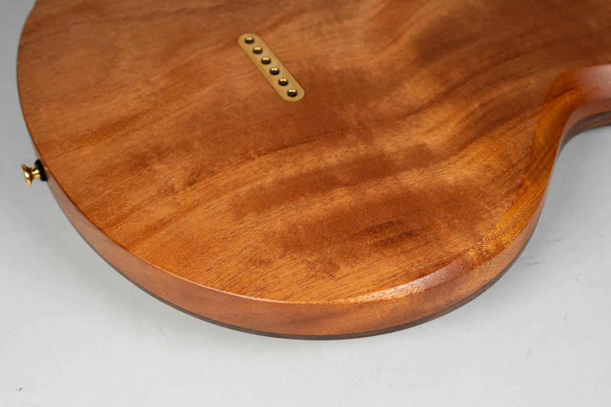 The guitar's figured walnut back, with a satin finish, shows a gold string-through-body ferrule plate and a gold strap button.