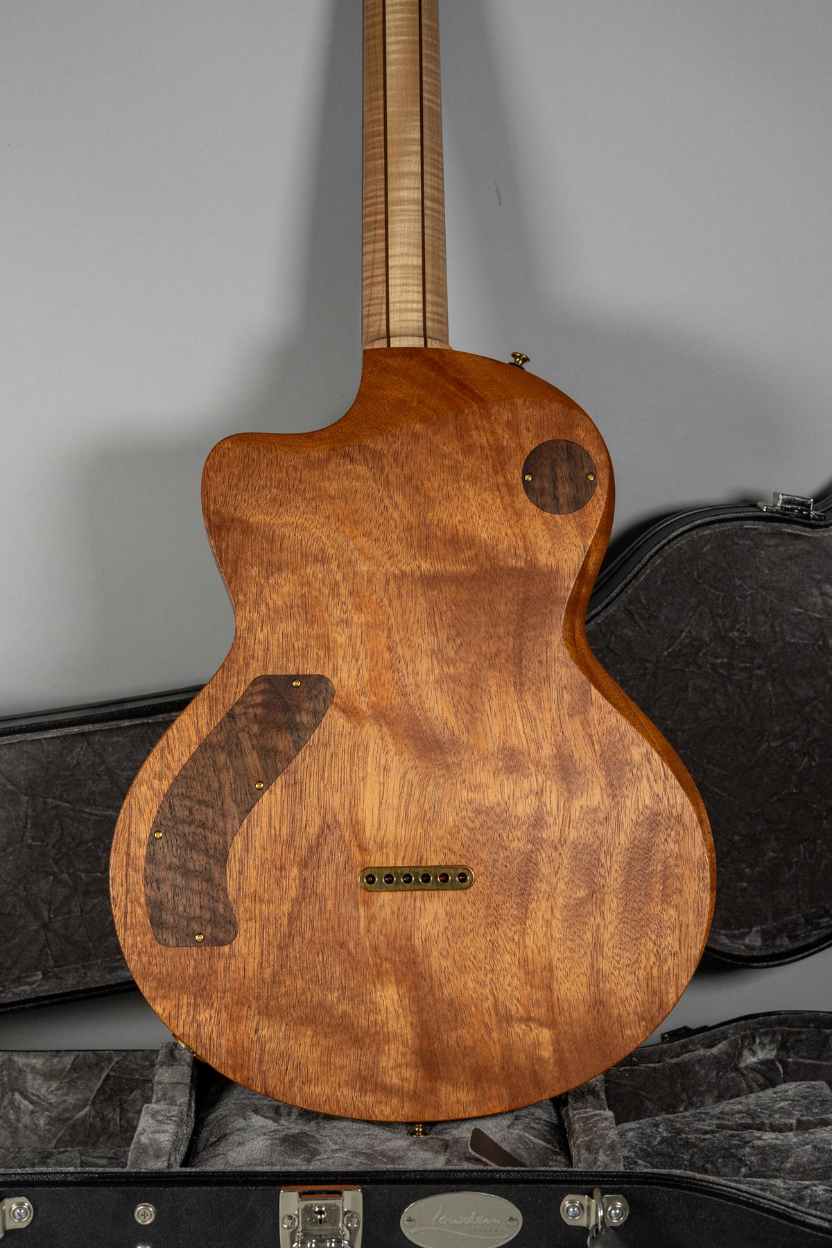 The guitar's back, a warm brown wood with visible grain, features two dark walnut control plates and a gold string-through bridge.