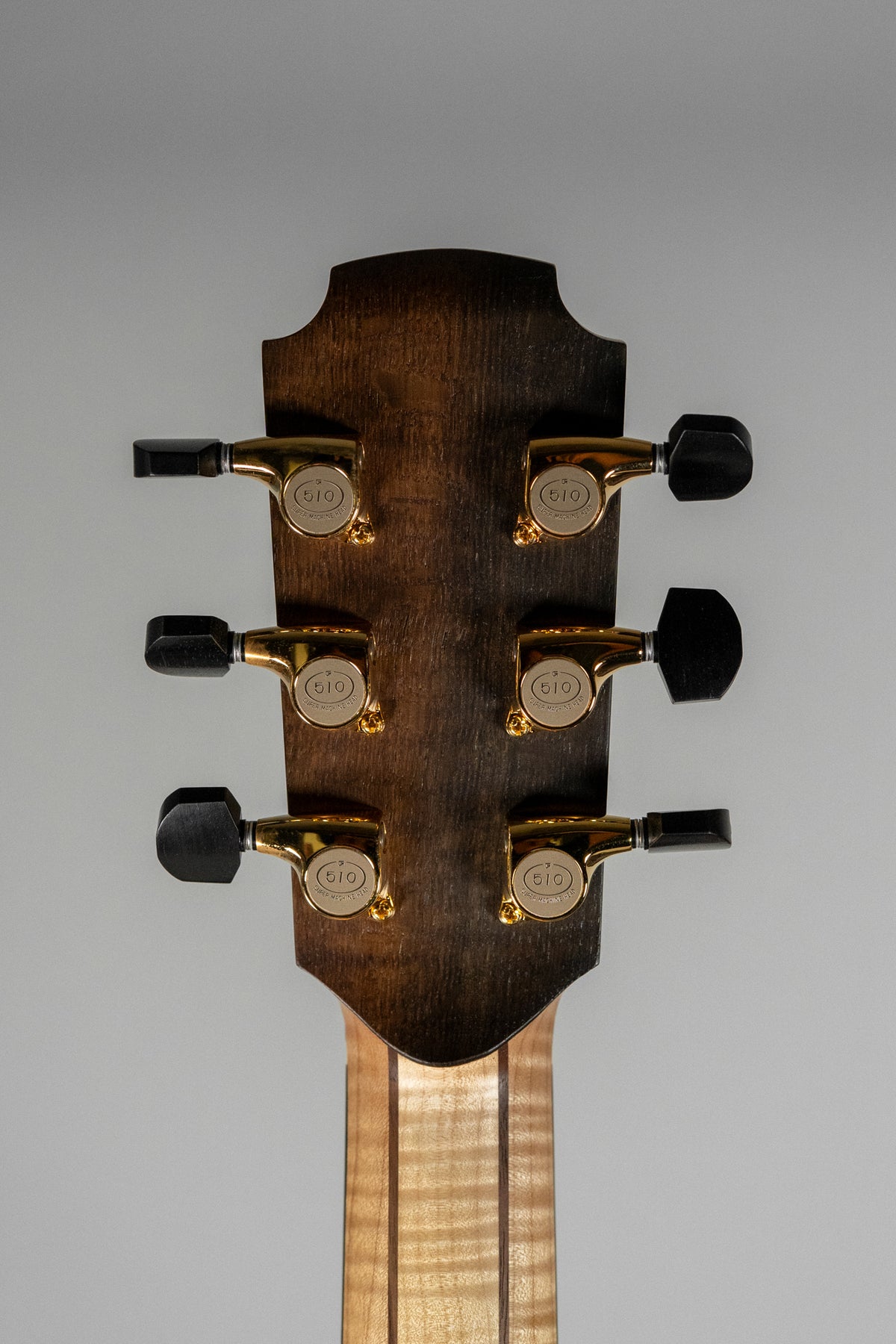 Rear view of the guitar's dark walnut headstock with six gold tuners and black buttons, above a flamed maple neck.