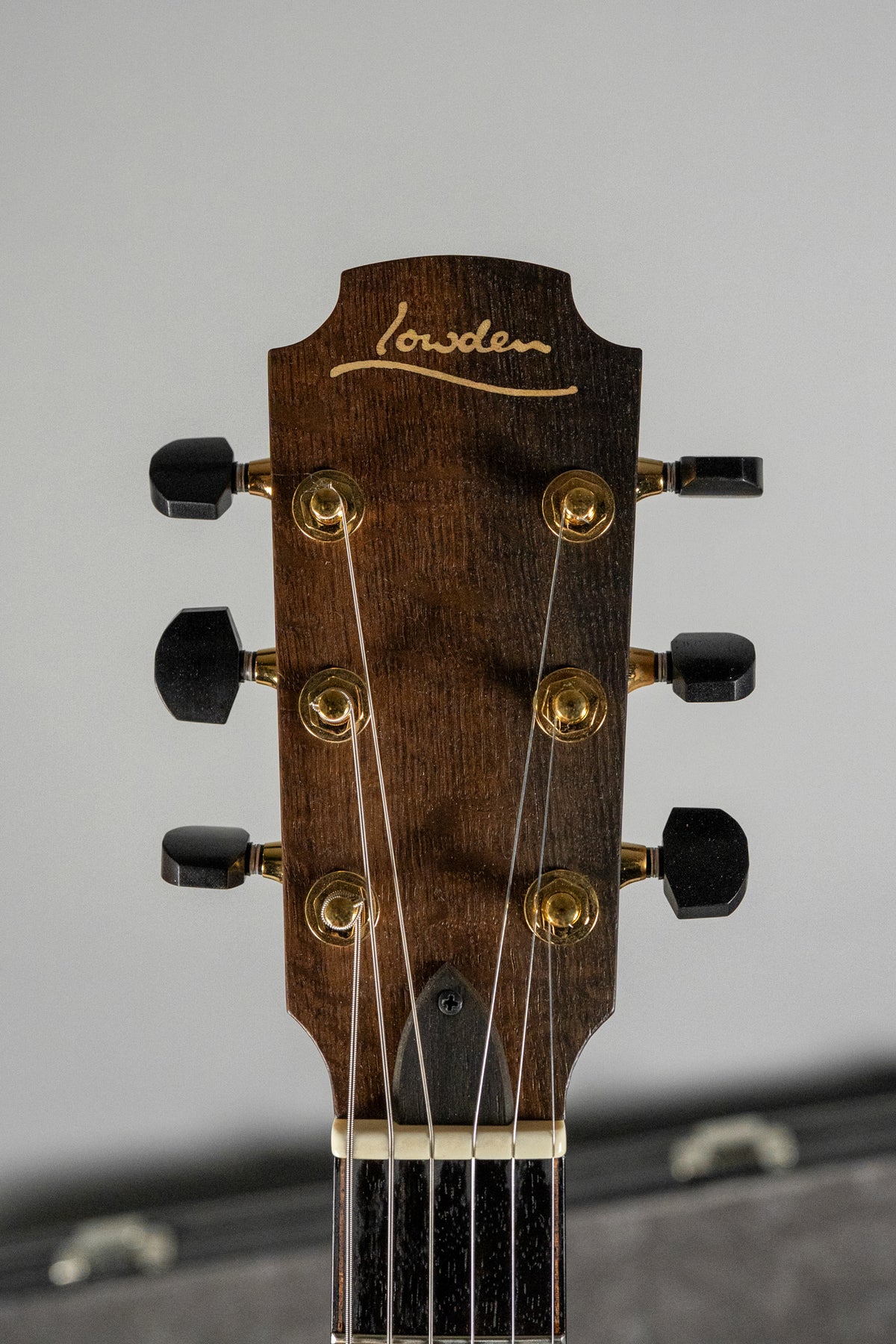 Close-up of the dark figured walnut headstock with gold tuners and black buttons, showing the top of the fretboard and nut.